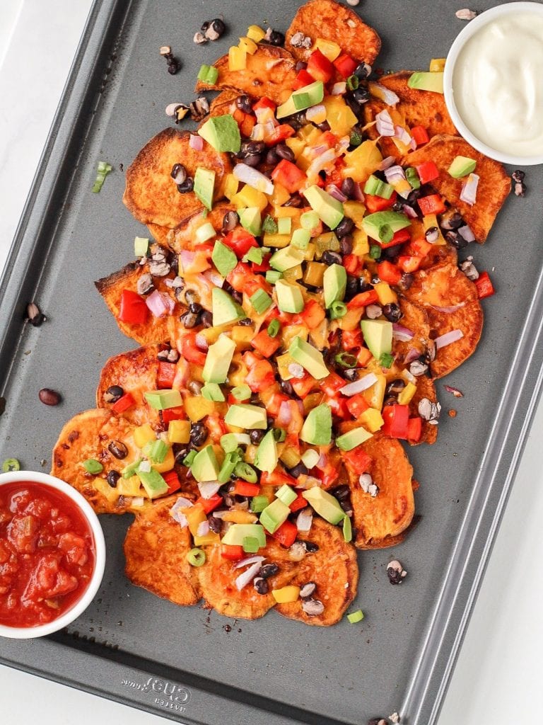 sweet potato nachos on a sheet pan topped with vegetables, beans and cheese