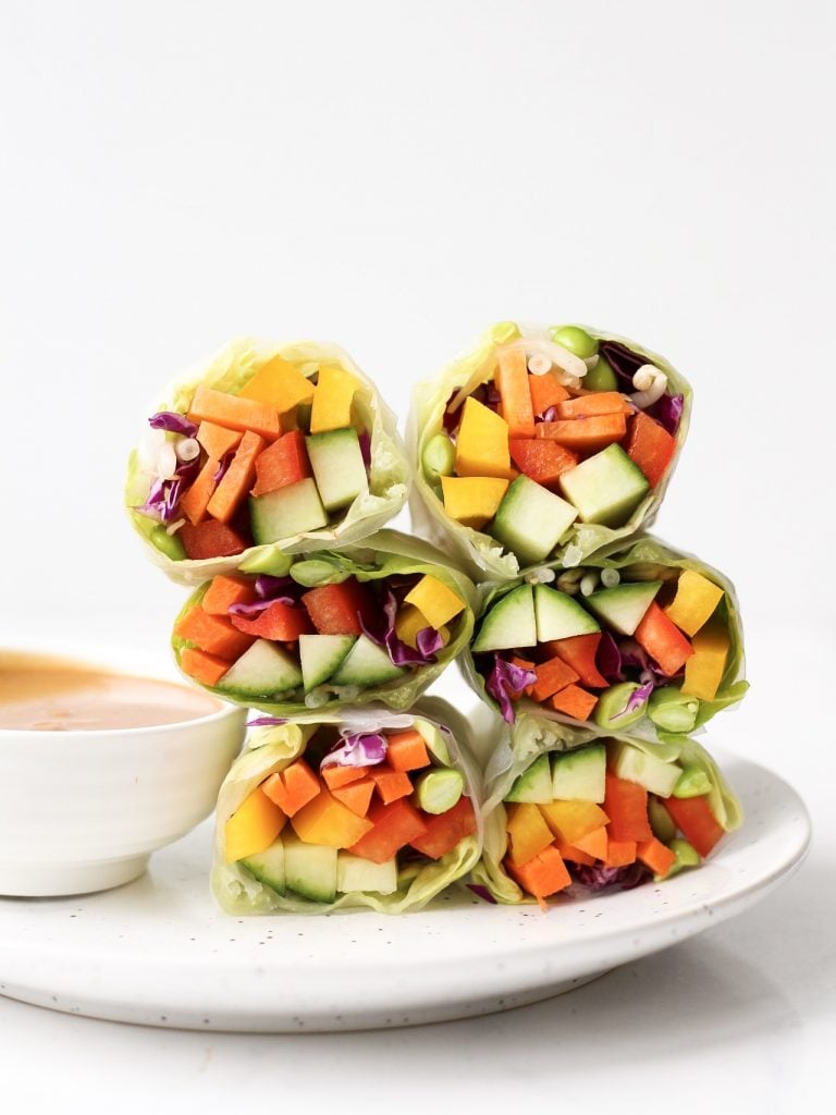 Vegetable-filled rice paper rolls stacked on a white plate