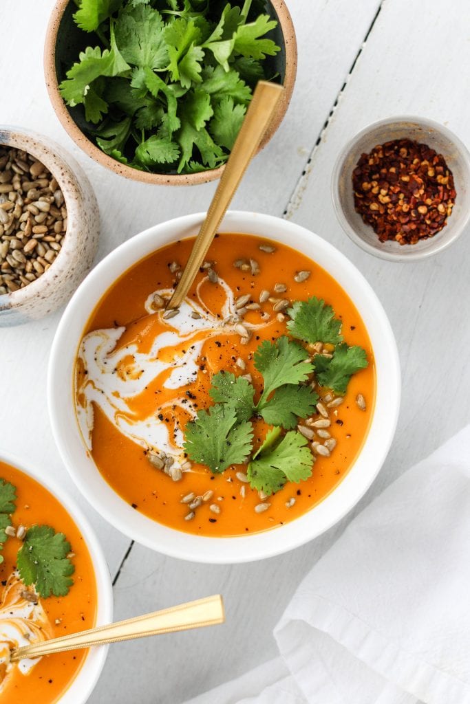 Spicy butternut squash and sweet potato soup in a white bowl garnished with cilantro, coconut cream and sunflower seeds.