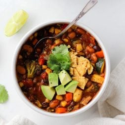 Vegetarian chili in a white bowl with a silver spoon on a white marble surface.