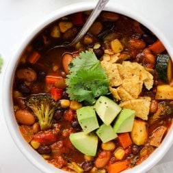 Veggie chili in a white bowl with a silver spoon on a white marble surface