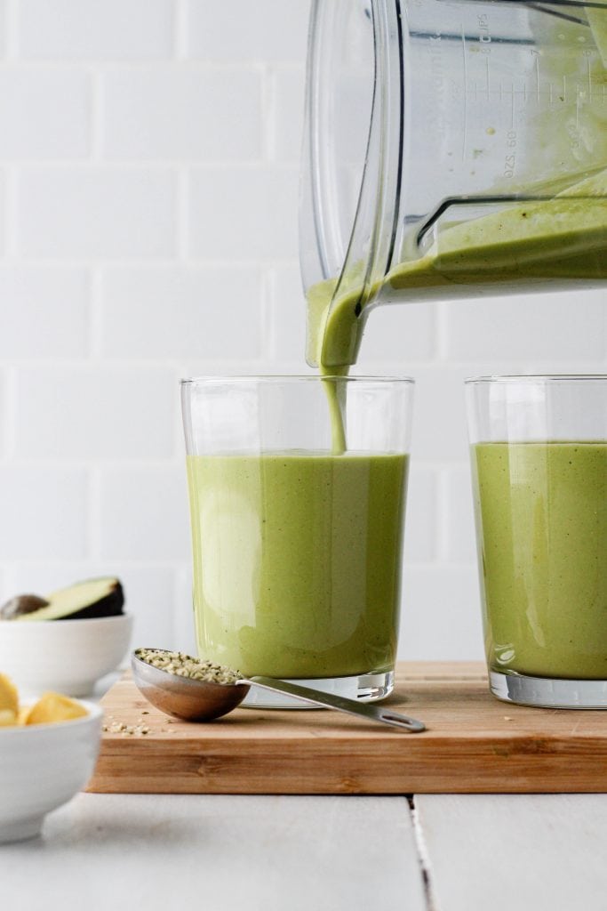 Green smoothie being poured into a glass in front of a white background