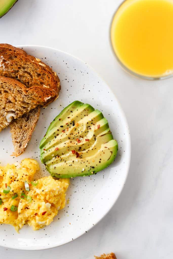 A balanced breakfast plate with whole grain toast, scrambled eggs, avocado, and orange juice.