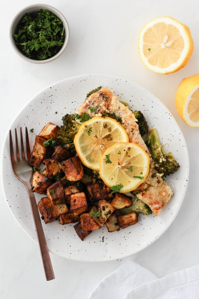 Baked lemon butter haddock on a plate with broccoli and roasted potatoes