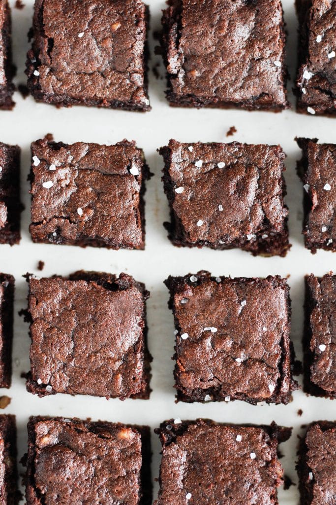 An overhead view of brownies lined up on a white marble surface. The brownies are sprinkled with flaky sea salt.