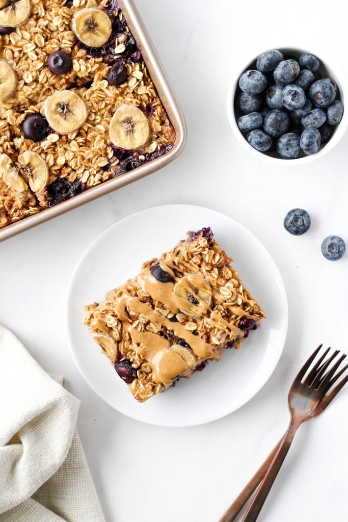Baked oatmeal with blueberries and bananas on a plate drizzled with peanut butter