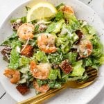 Make a restaurant-style Caesar Salad at home! This Healthy Caesar Salad recipe is made with crisp romaine, homemade croutons, a homemade creamy caesar dressing and optional lemon garlic shrimp.
