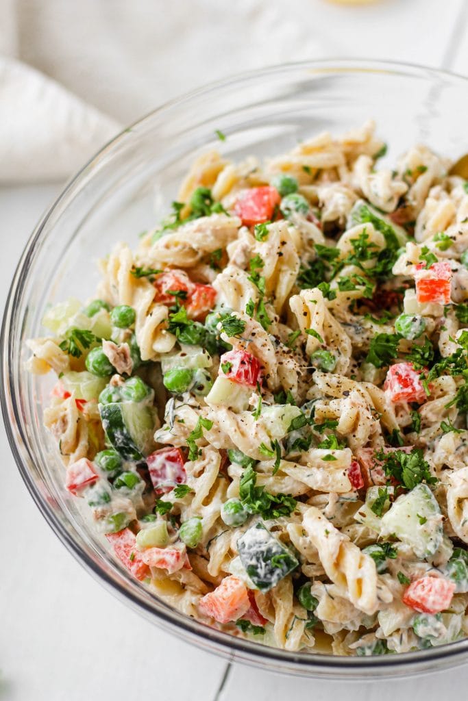 A creamy, healthy tuna pasta salad in a large bowl made with whole grain rotini, red bell pepper, cucumber, celery, green peas, and a creamy greek yogurt dill dressing. 