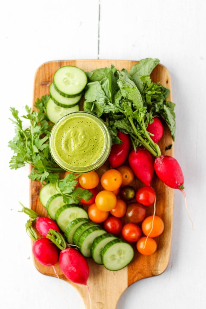 raw veggies on a wooden serving board with a jar of green goddess dressing for dipping