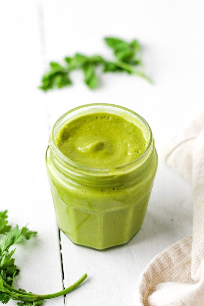 a jar of green goddess dressing on a white wooden surface
