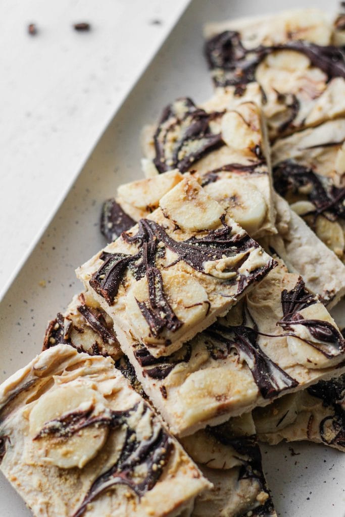 peanut butter greek yogurt bark swirled with chocolate and topped with banana on a plate