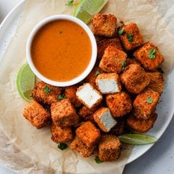 Tofu nuggets on a plate lined with parchment paper, served with dip