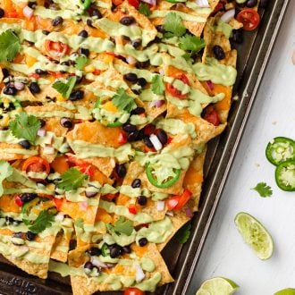 Sheet pan of vegetarian nachos loaded with vegetables, beans, and cilantro avocado crema