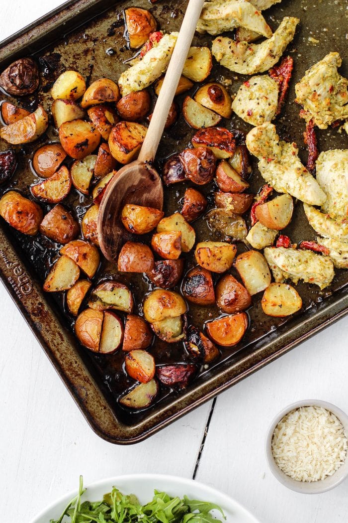 roasted potatoes and pesto chicken on a baking sheet