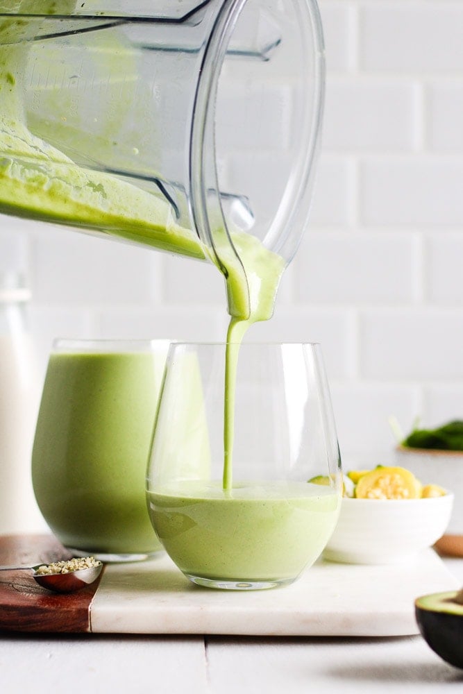 pouring green smoothie into a glass