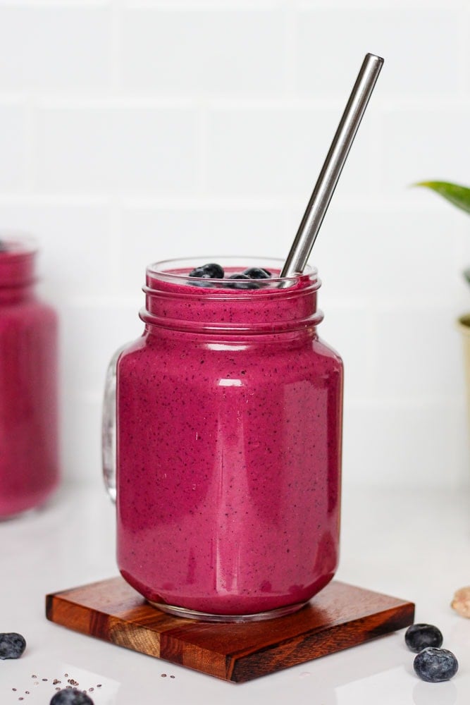 red beet smoothie in a mason jar with a straw and blueberries on top