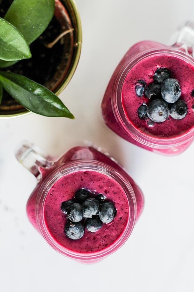 two blueberry beet smoothies in mason jars topped with blueberries