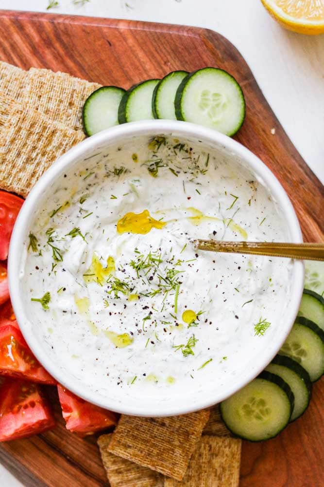 homemade tzatziki in a bowl on a serving board with cut up vegetables and crackers