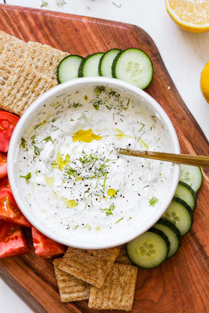 homemade tzatziki in a bowl on a serving board with cut up vegetables and crackers