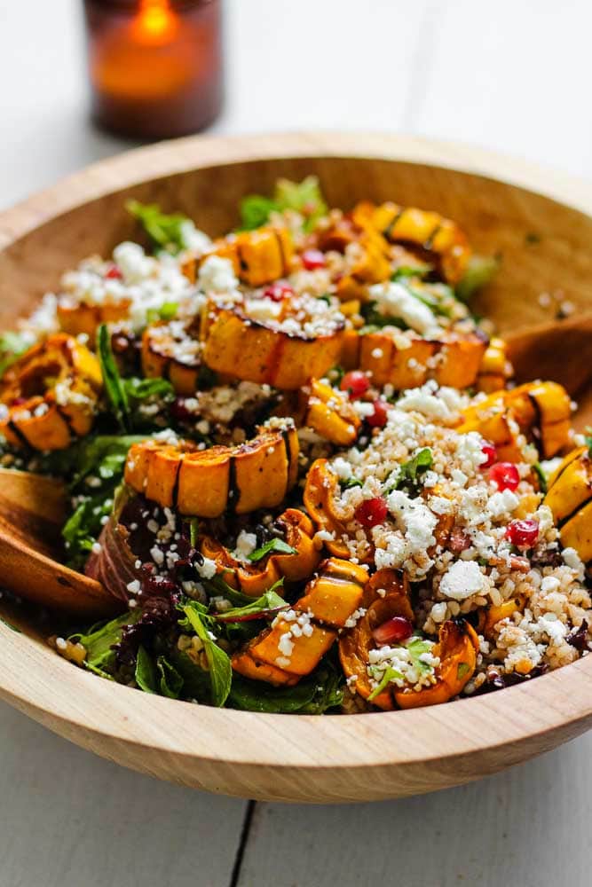 roasted delicata squash in a salad with greens, pomegranate seeds, goat cheese and walnuts
