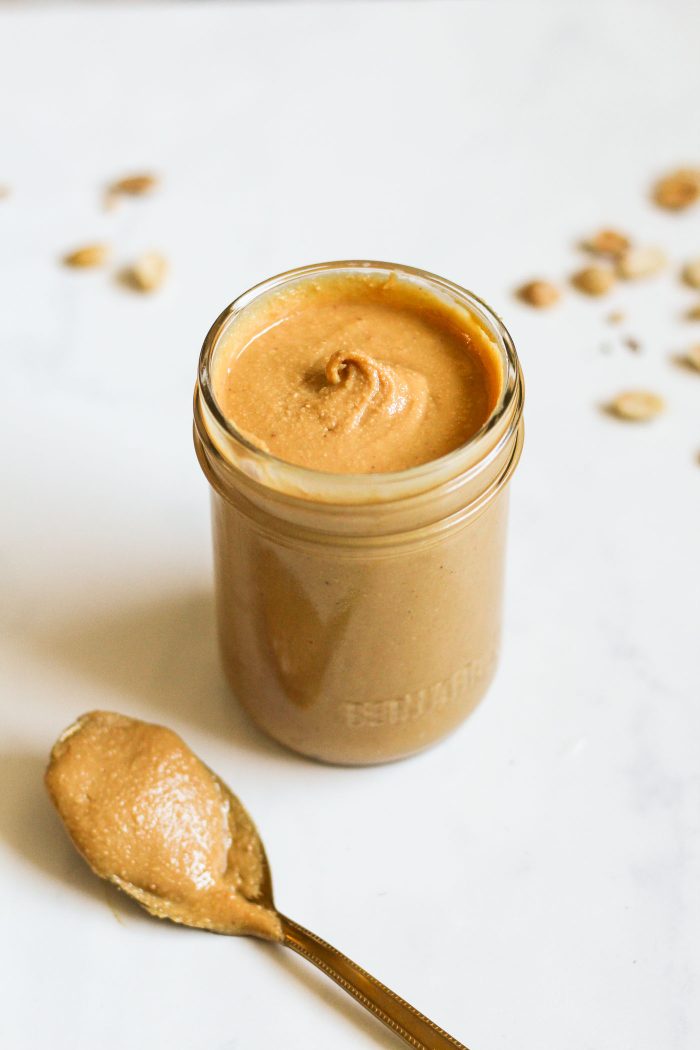 homemade peanut butter in a jar beside a spoon with peanut butter on it