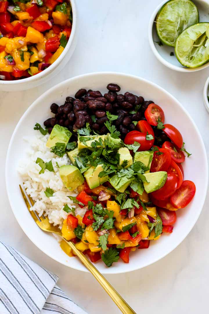 bowl of rice and black beans topped with sliced grape tomatoes, mango salsa, avocado, and cilantro