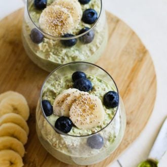 two jars of matcha overnight oats topped with blueberries, sliced banana, and chia seeds