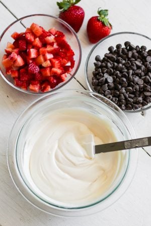 greek yogurt in a bowl beside bowls of strawberries and chocolate chips
