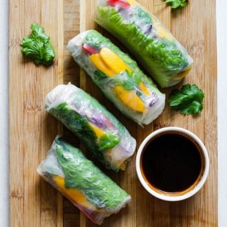 rice paper rolls on a wooden board with a dish of dipping sauce
