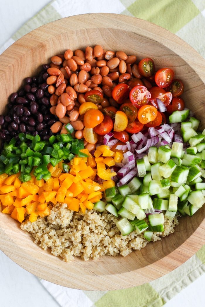 large salad bowl with cooked quinoa, black beans, pinto beans, and diced vegetables
