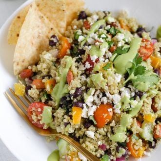 quinoa salad with black beans, pinto beans, and vegetables in a bowl topped with green avocado dressing