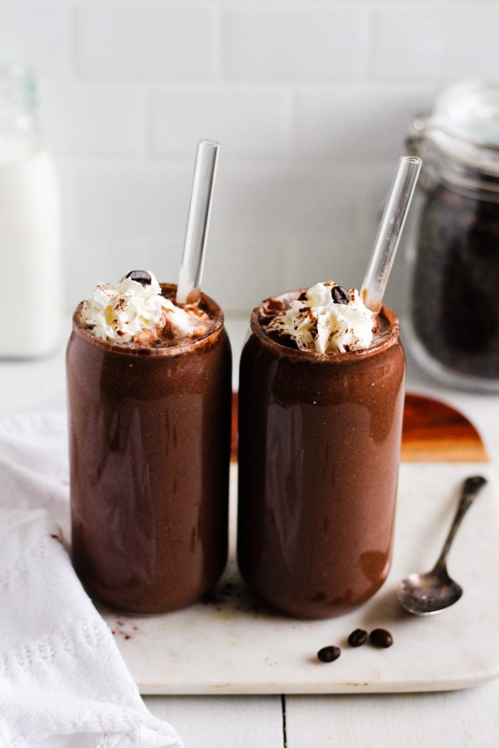 two glasses of a dark brown chocolate coffee smoothie topped with whipped cream and coffee beans