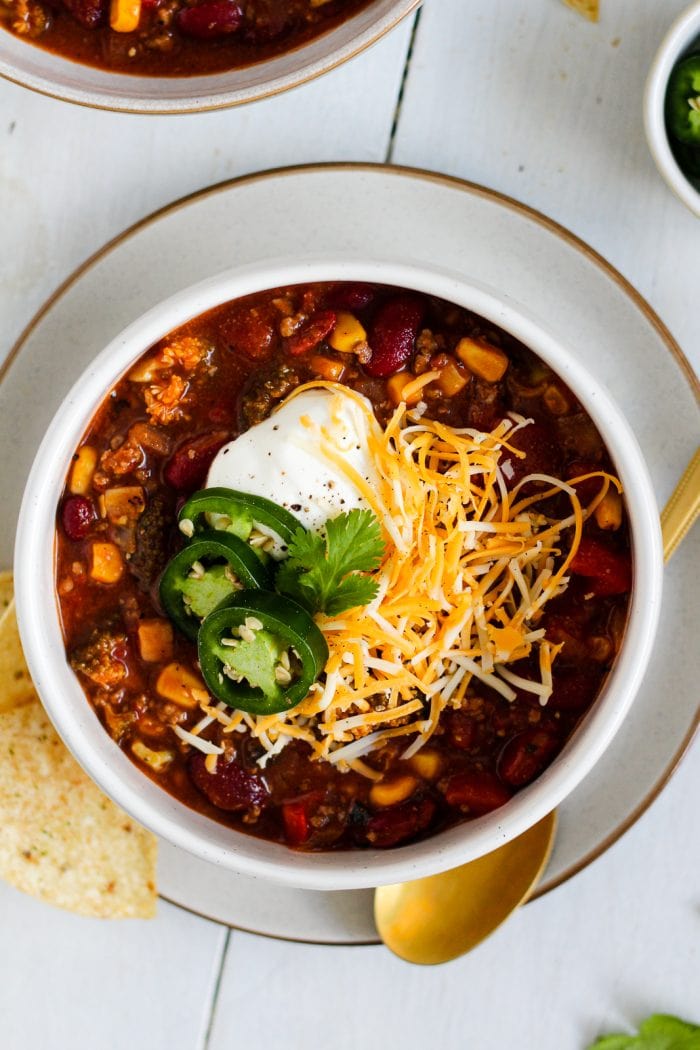 bowl of chili topped with plain greek yogurt, shredded cheese, and jalapeno slices with a side of tortilla chips