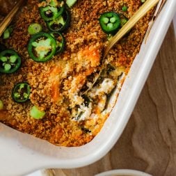 Baking dish with jalapeno popper dip being dipped into with a spoon