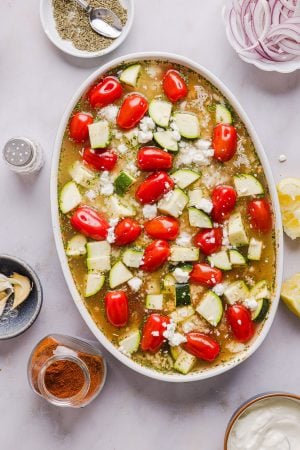 zucchini, tomatoes, and feta on top of a casserole mixture in a casserole dish