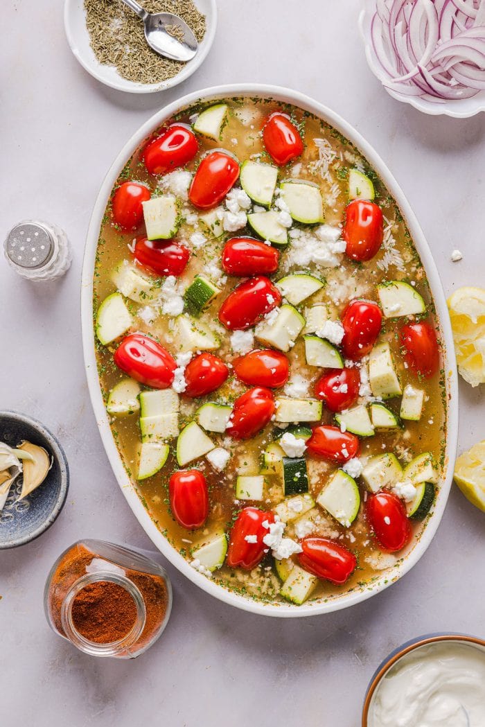 zucchini, tomatoes, and feta on top of a casserole mixture in a casserole dish