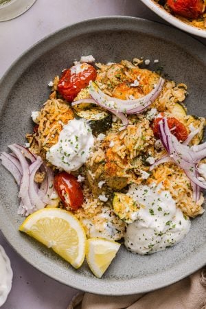 greek chicken and rice casserole served in a bowl and topped with sliced red onion and feta cheese