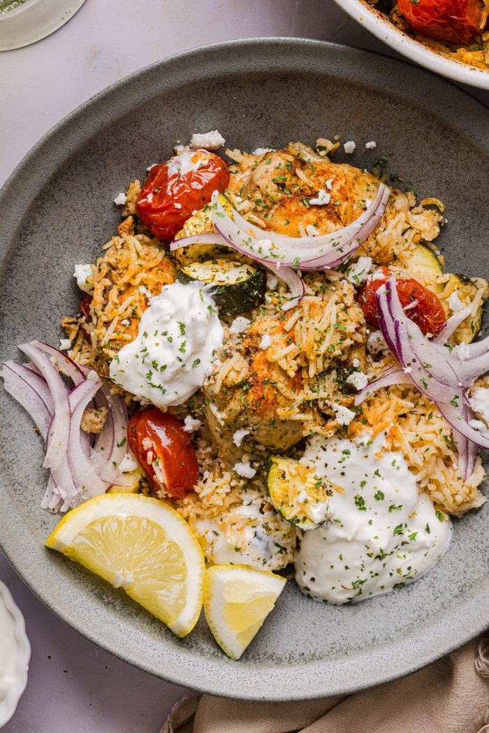 greek chicken and rice casserole served in a bowl and topped with sliced red onion and feta cheese