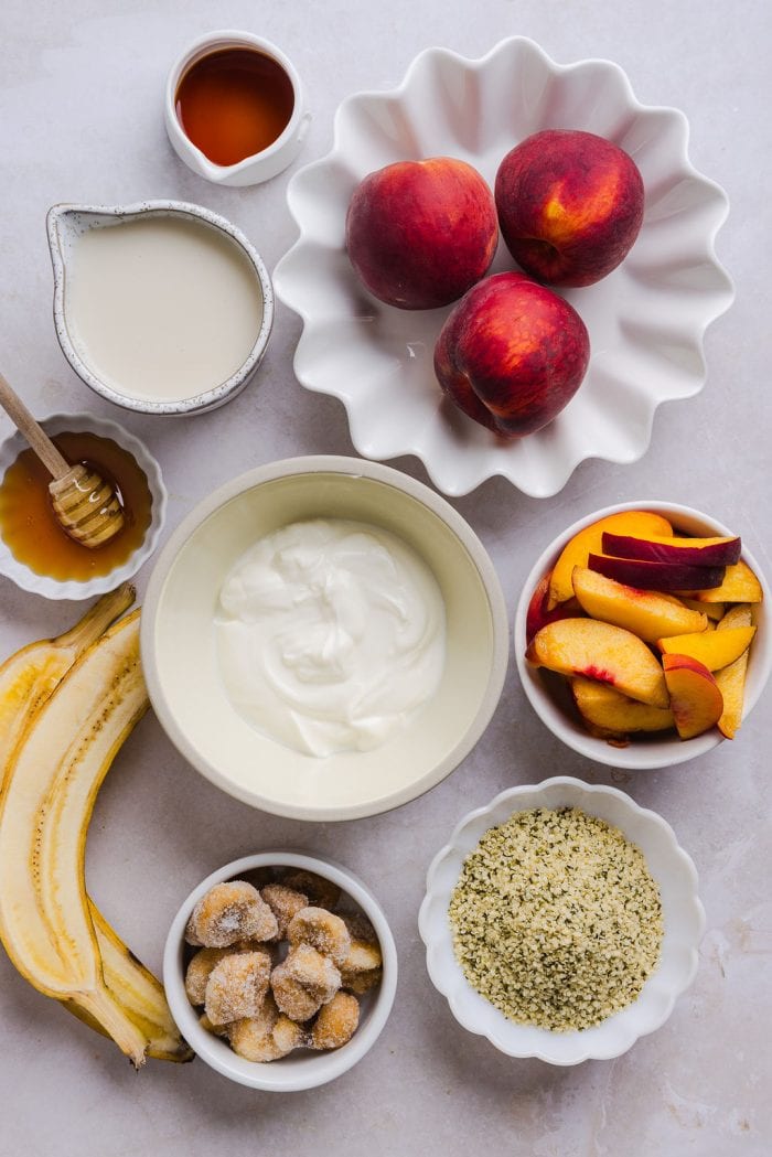 ingredients for a peach banana smoothie including greek yogurt, hemp seeds, honey, and vanilla