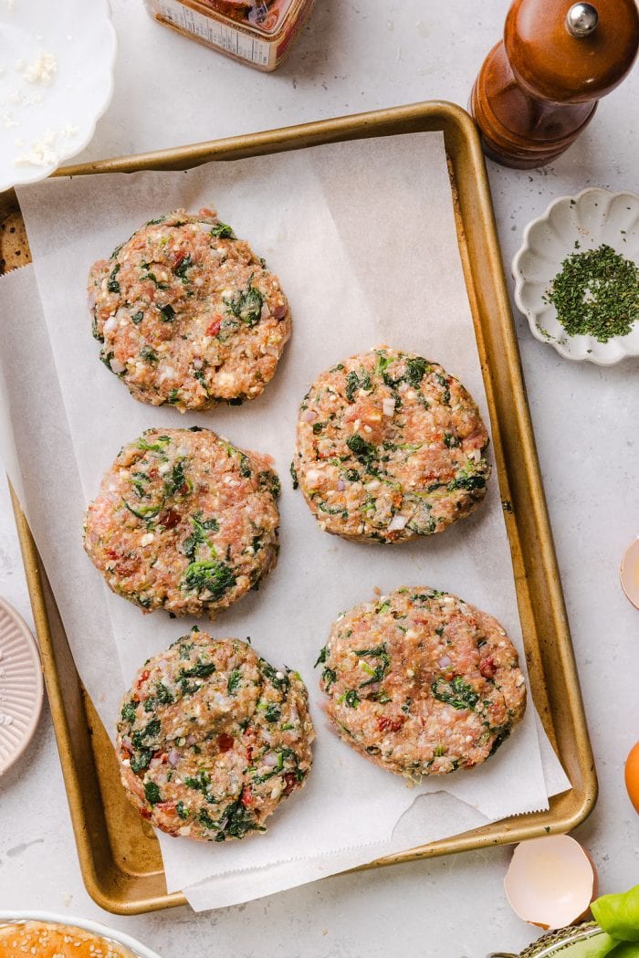 five spinach feta turkey burger patties on a parchment-lined pan